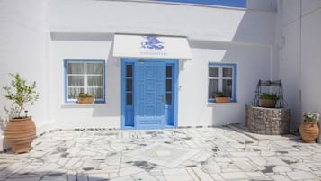 A building with a blue door and windows, potted plants, and a stone-tiled courtyard.