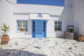 A building with a blue door and windows, potted plants, and a stone-tiled courtyard. - Hotel Saint George Valsamitis (Amorgos)