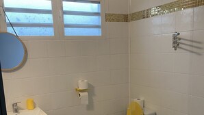 A bathroom with a toilet, sink, and mirror. There are two windows above the toilet. - Functional holiday home 2 minutes from the beach (Ste anne)