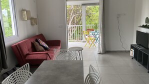 A modern living room with a red sofa, white chairs, a grey table, and a TV on a stand. - Functional holiday home 2 minutes from the beach (Ste anne)