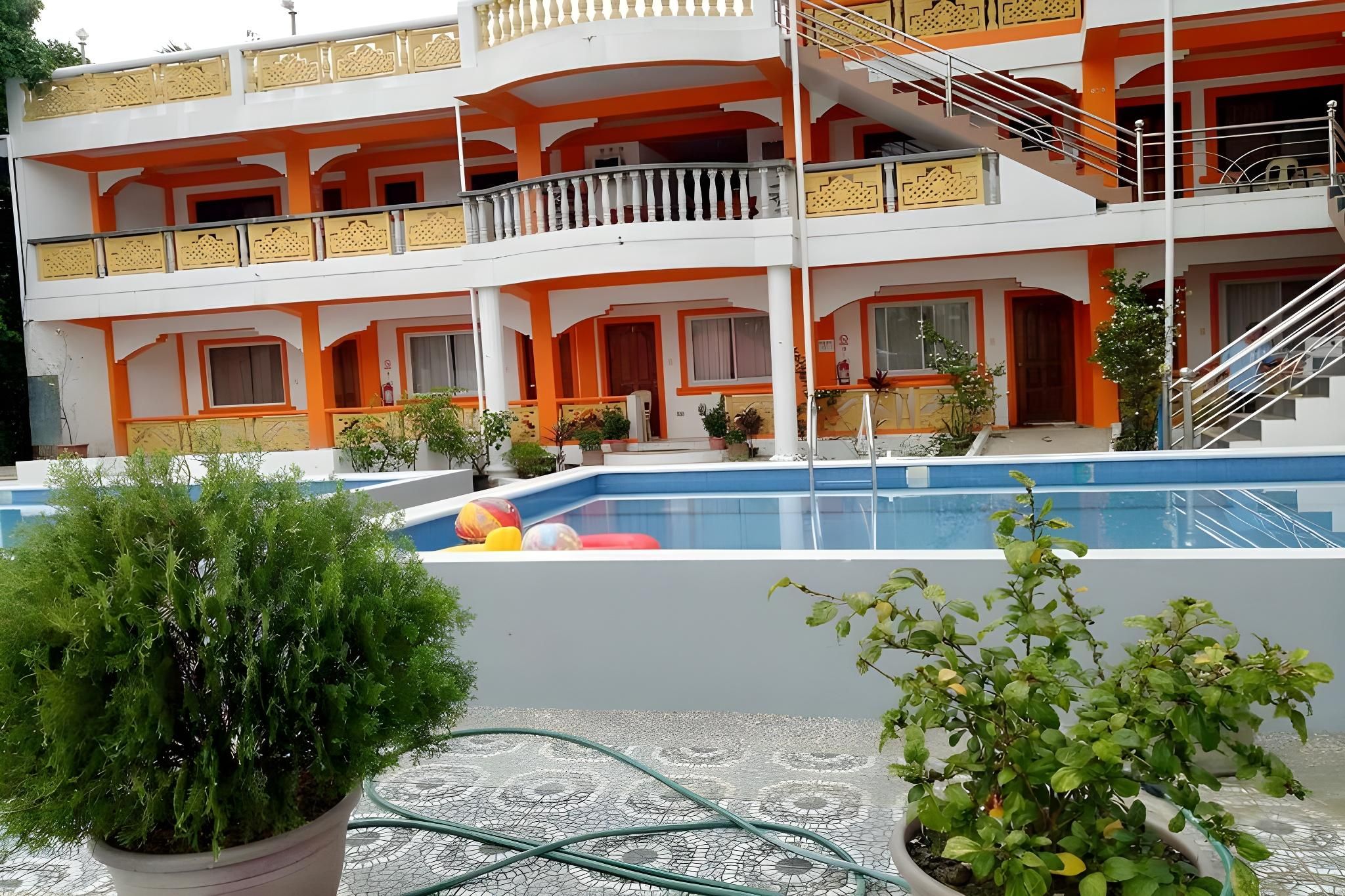 Un hotel de varios pisos con piscina, balcones y plantas en macetas.