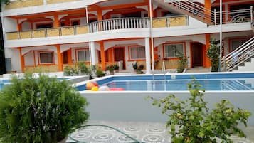 Un hotel de varios pisos con piscina, balcones y plantas en macetas.