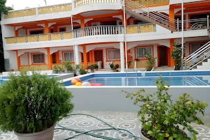 A multi-story hotel with a swimming pool, balconies, and potted plants.
