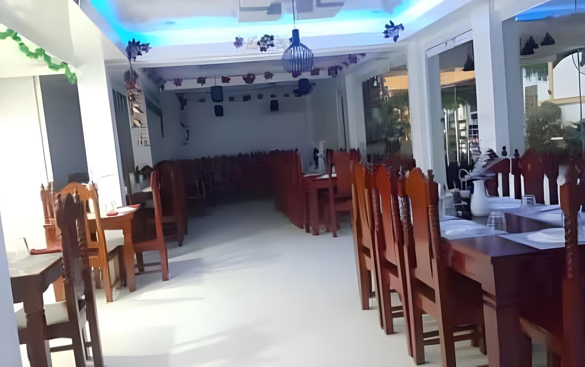 Un comedor con mesas y sillas de madera, piso blanco y techo con una lámpara.