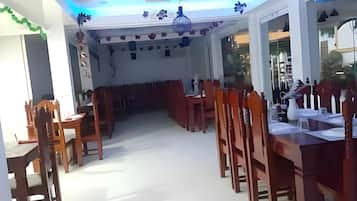 Un comedor con mesas y sillas de madera, piso blanco y techo con una lámpara.