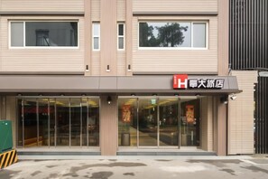 L’entrée d’un hôtel, avec une façade moderne, de grandes fenêtres en verre et une enseigne bien visible.