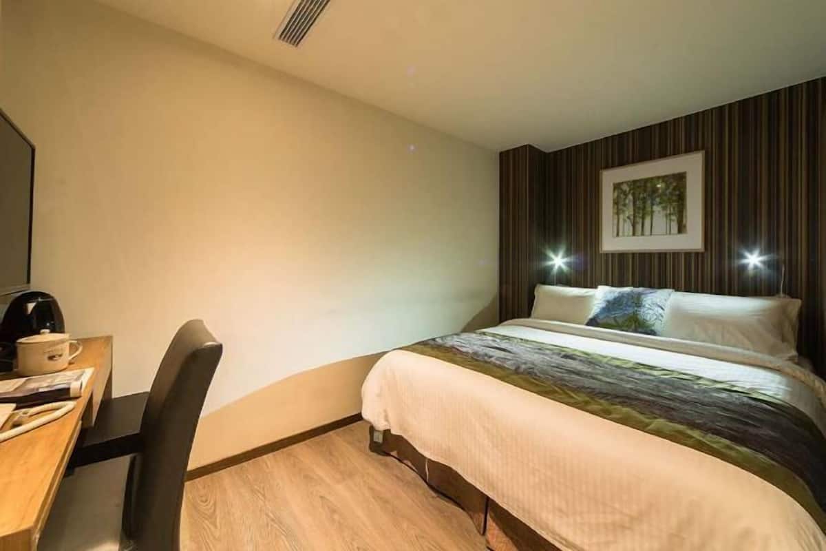 A hotel room with a bed, a desk with a chair, a coffee maker, and a framed picture on the wall.