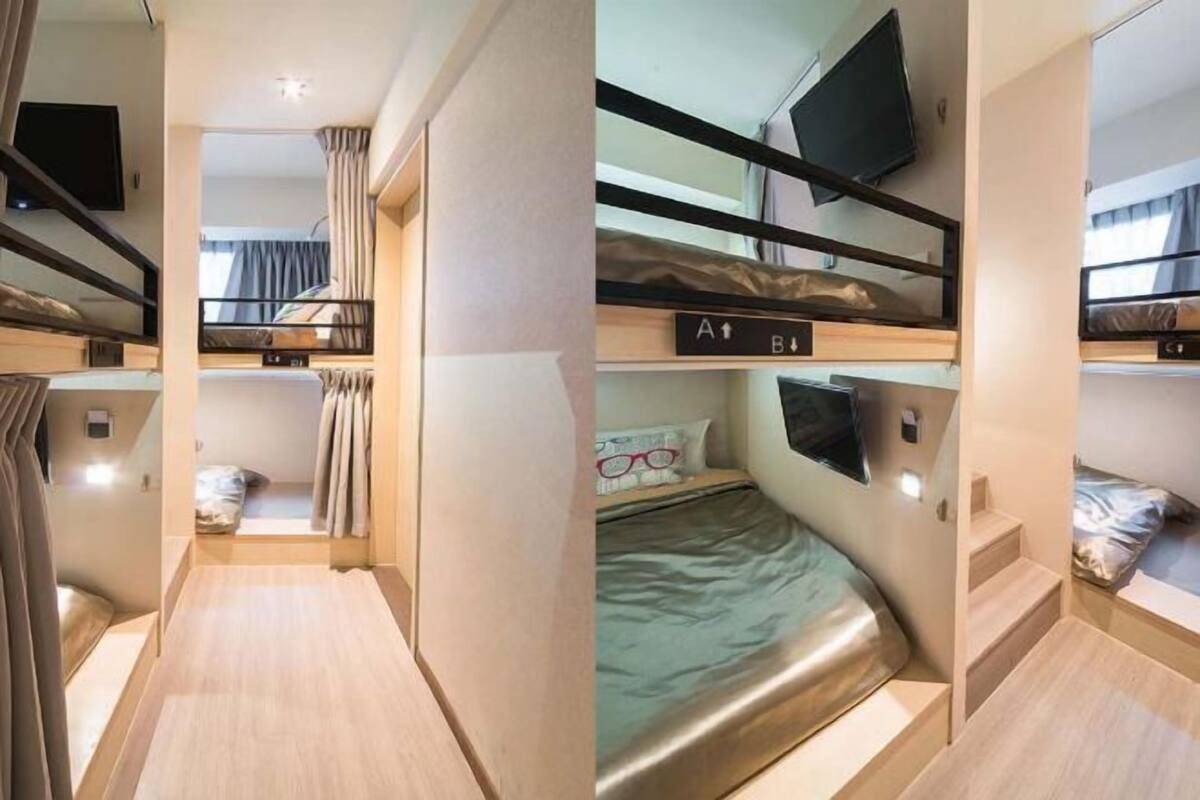 A bunk bed room with a television above the upper bunk, a small window with curtains, and a sign indicating the direction to the bathroom.