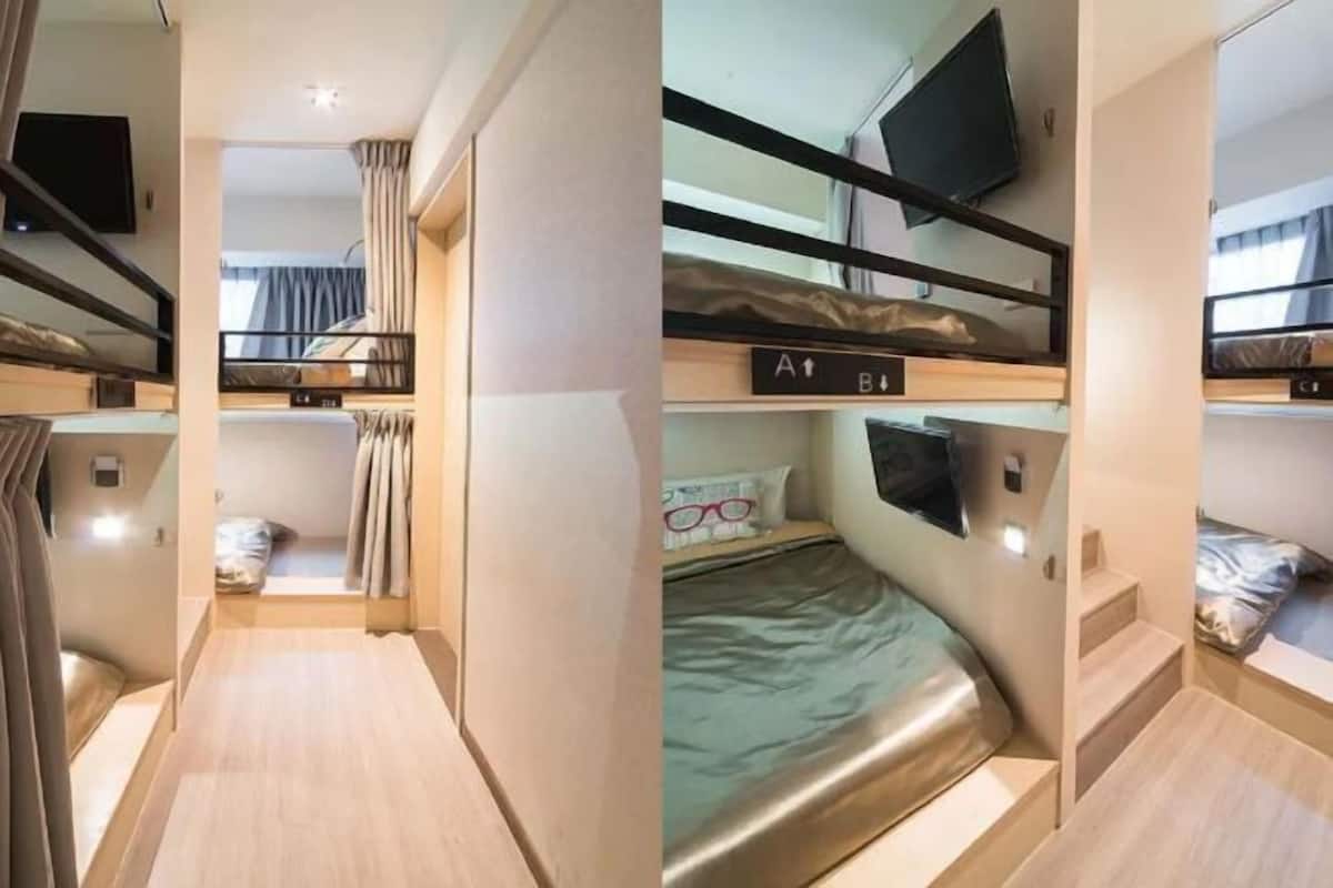 A bunk bed room with a television above the upper bunk, a small window, and a wooden floor.