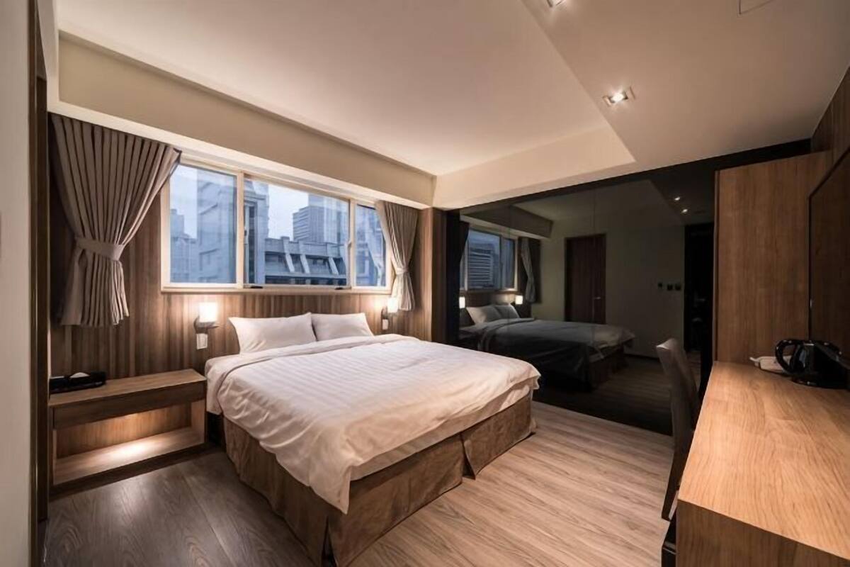 A modern bedroom with a large bed, bedside tables, a desk, and a view of the city.