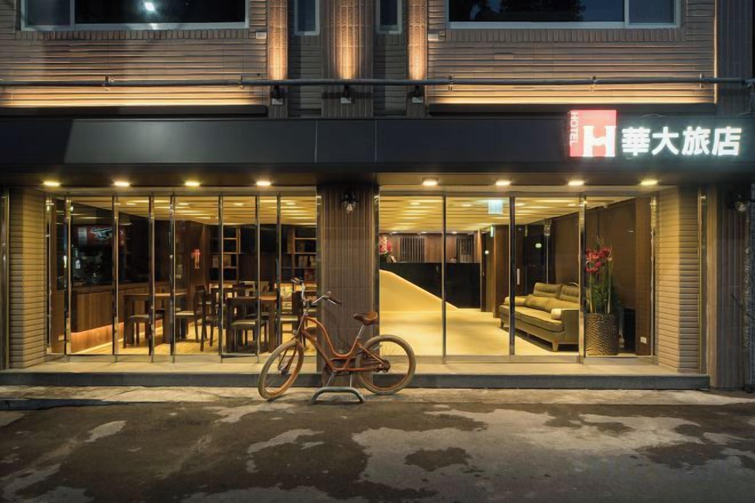 Entrada de un hotel con una bicicleta estacionada afuera, un área de descanso en el interior y un letrero con caracteres chinos.