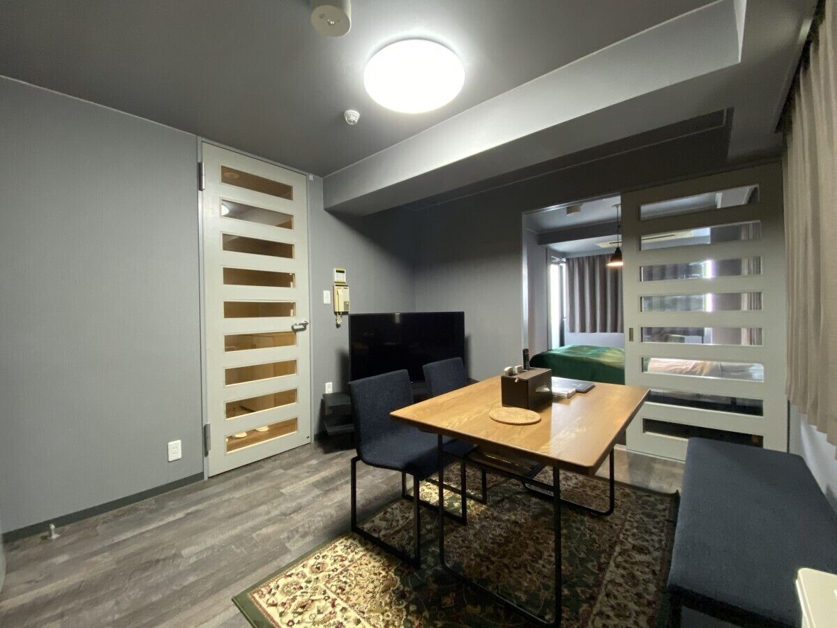 Habitación compacta con una mesa de madera, dos sillas, un sofá, un televisor y un armario con puerta corredera.