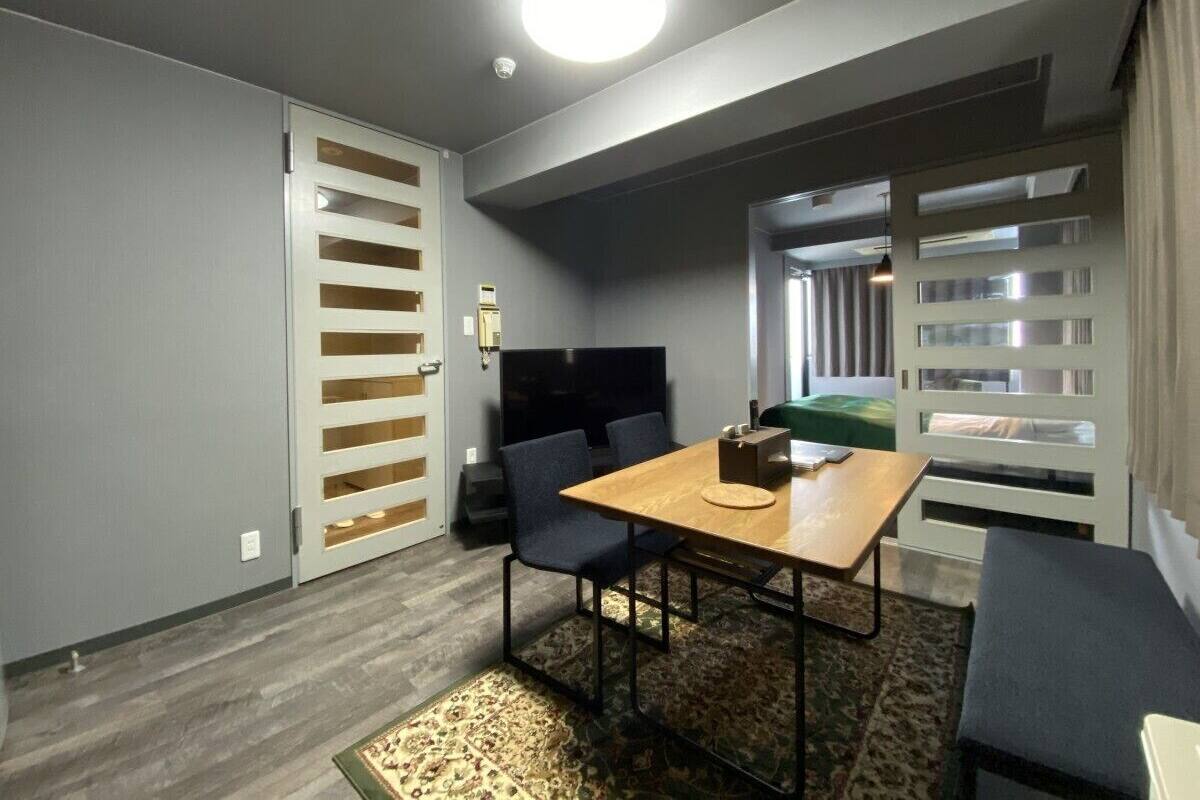 A compact room with a wooden table, two chairs, a sofa, a TV, and a wardrobe with a sliding door.