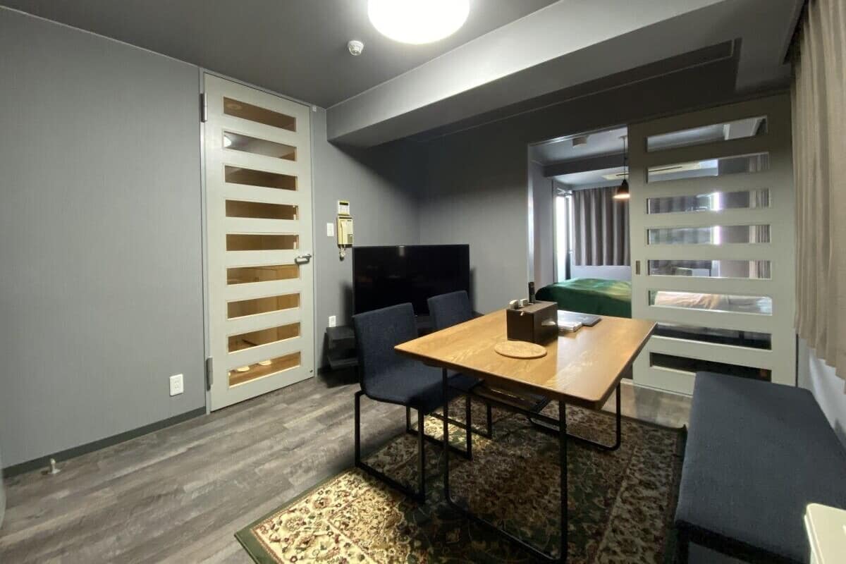 Habitación compacta con una mesa de madera, dos sillas, un sofá, un televisor y un armario con puerta corredera.
