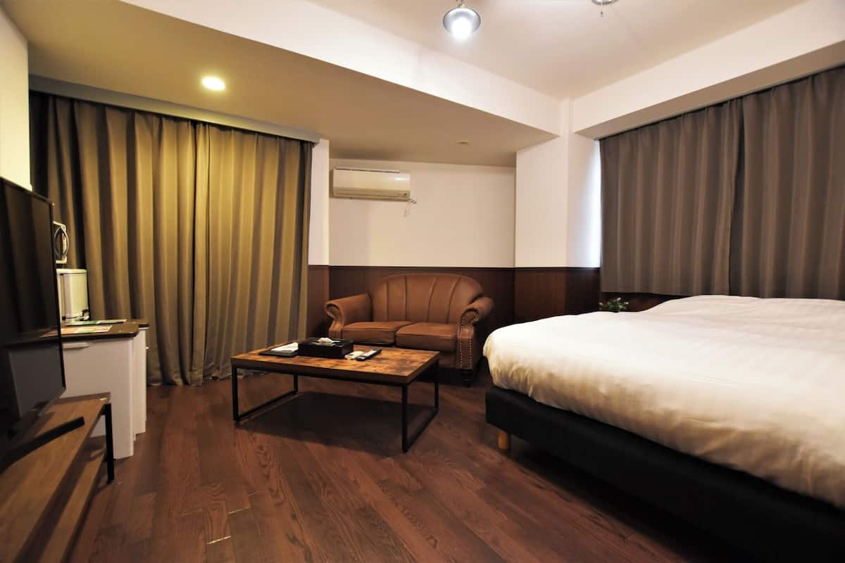 A hotel room with a bed, a desk, a chair, a coffee table, and a television.