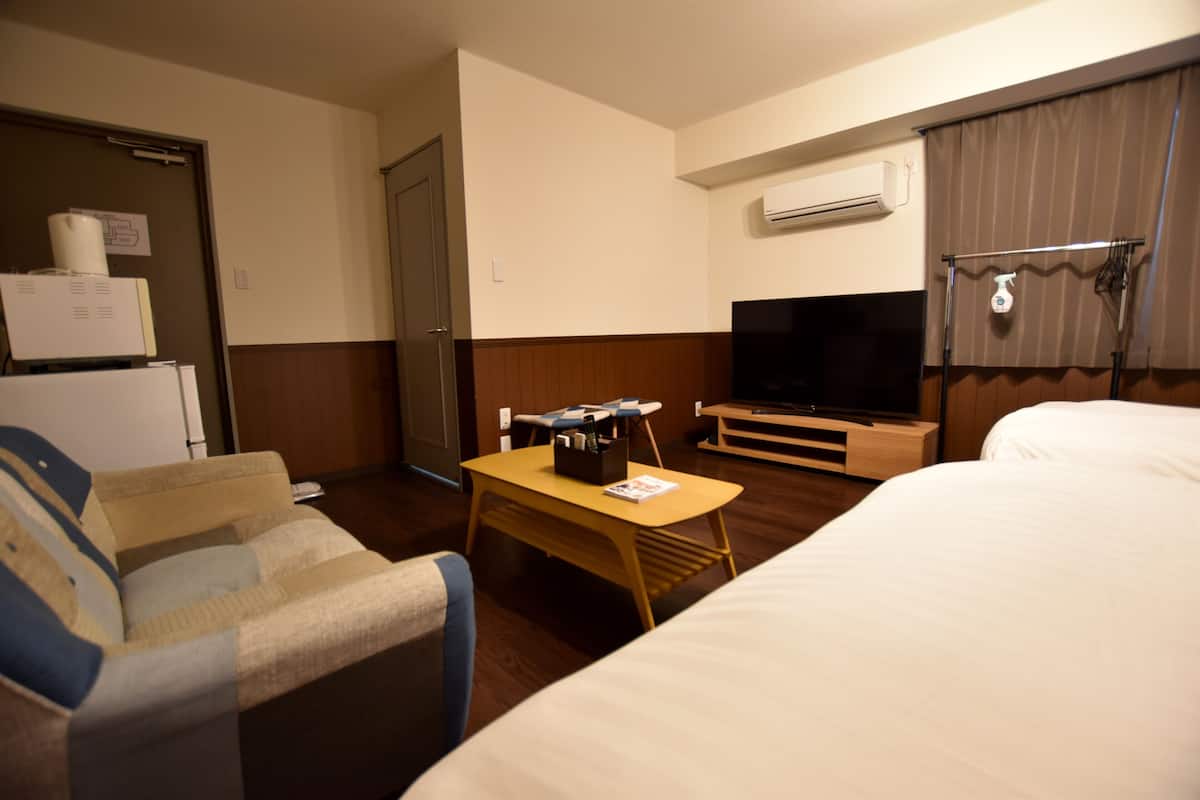 A hotel room with a bed, a television, a small table, a chair, and a refrigerator.
