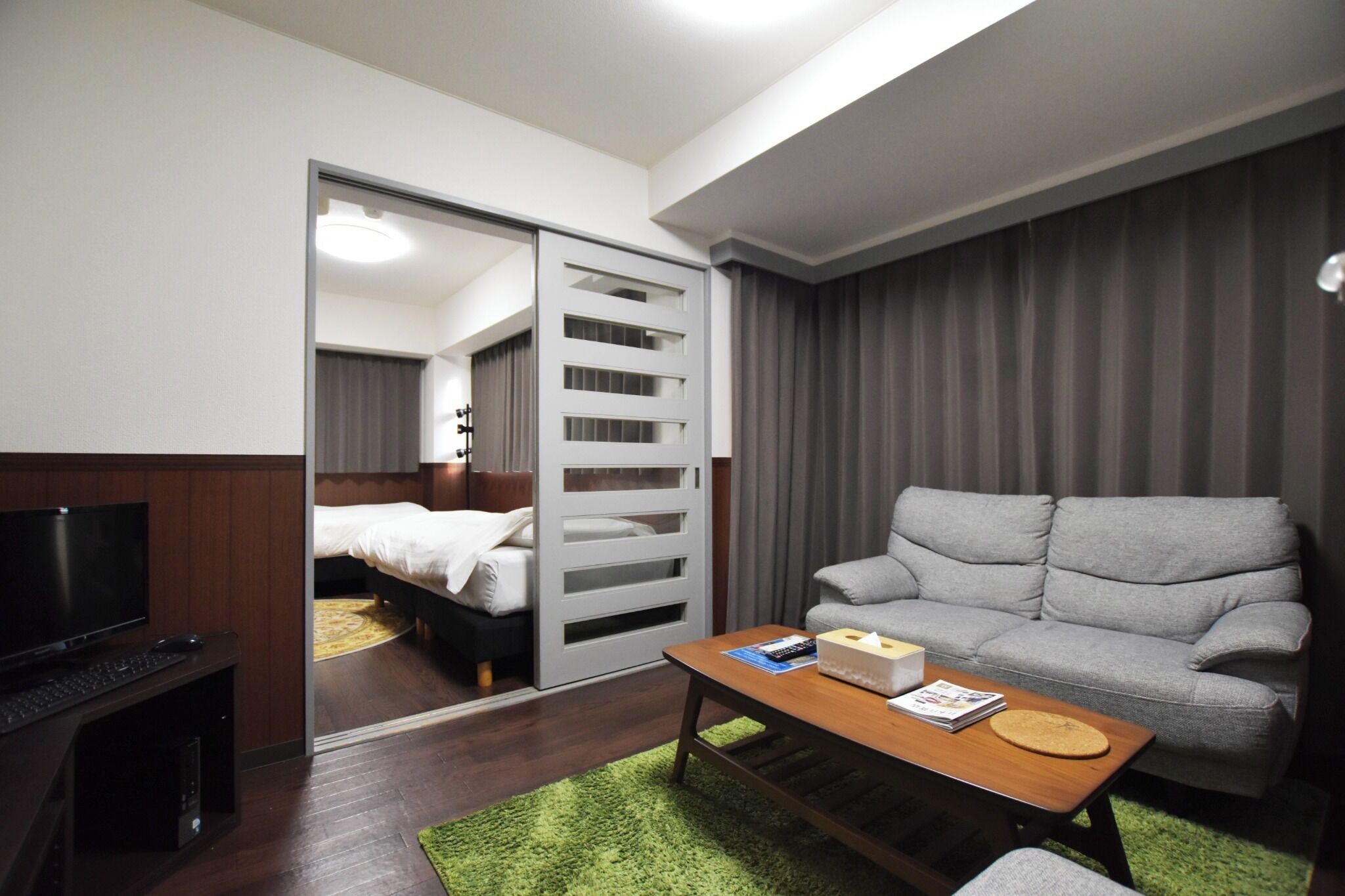 A hotel room with a bed, a television, a sofa, a coffee table, and a sliding door leading to another room.