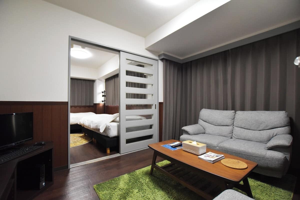 A hotel room with a bed, a television, a sofa, a coffee table, and a sliding door leading to another room.