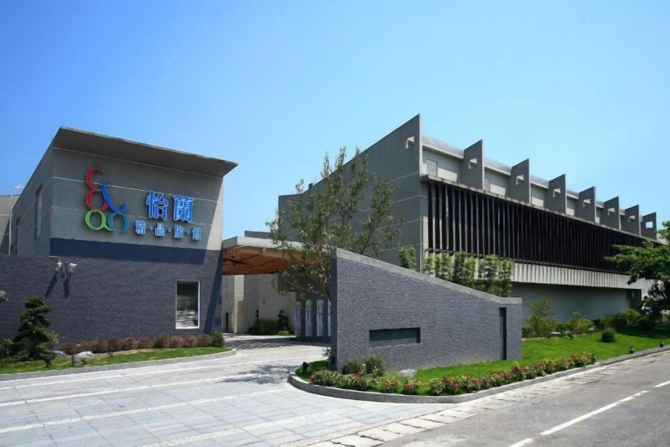 A modern building with a prominent sign, a paved entrance, and a landscaped area with trees and shrubs.