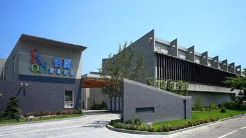 A modern building with a prominent sign, a paved entrance, and a landscaped area with trees and shrubs.