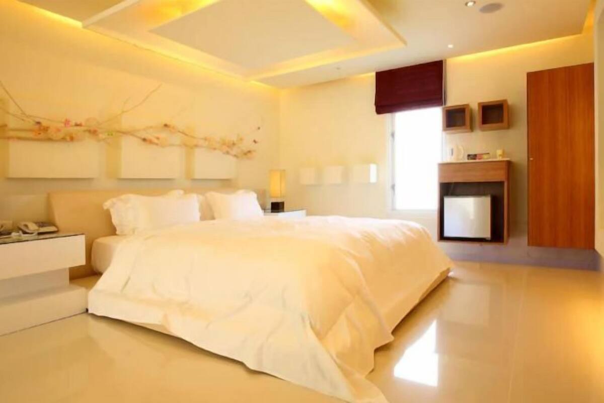 A modern bedroom with a large bed, bedside tables, a nightstand, a wall-mounted TV, and a fireplace.