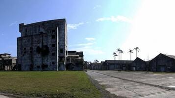 A large, multi-story building with a flat roof, surrounded by a grassy area and smaller structures.