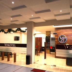 A hotel reception area with a wooden reception desk, a TV mounted on the wall, and a sign that reads 'YOKOTEL'. - Yokotel Hotel (Bandung)