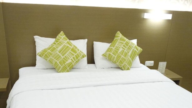 A neatly made bed with white bedding and two green patterned pillows. - Yokotel Hotel (Bandung)