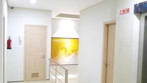 A hallway with an EXIT sign, a fire extinguisher, and a wall-mounted poster. - Yokotel Hotel (Bandung)