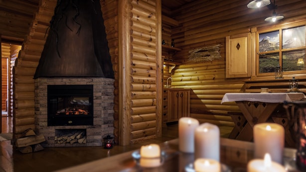 A log cabin interior with a stone fireplace, wooden walls, and a table with candles. - Sonya Hotel (Kyiv)