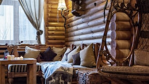 A cozy log cabin interior with a wooden log wall, a cushioned bench, a wicker chair, and a table with candles. - Sonya Hotel (Kyiv)