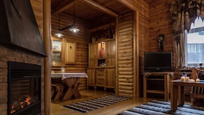A log cabin interior with a fireplace, wooden cabinets, a dining table, and a television. - Sonya Hotel (Kyiv)
