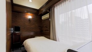 Ein Hotelzimmer mit einem Bett, einem Fernseher auf einem Tisch, einer Wandklimaanlage und einem Fenster mit durchsichtigen Vorhängen.