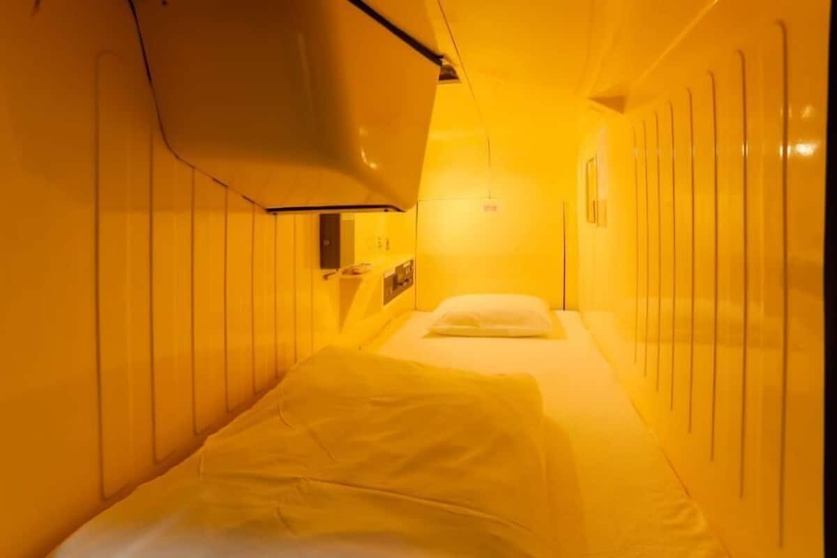 A narrow, yellow-lit corridor with a bed at the end.