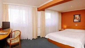A hotel room with a bed, a desk with a chair, a television, and curtains. - Dukla Presov (Prešov)