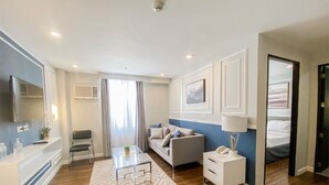 A modern hotel room with a sofa, a coffee table, a TV, a bedside table with a lamp, and a bed. - Uncle Tom's Cabin Hotel (Cebu City)