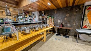 A buffet setup with stainless steel serving dishes, a wooden table, and a stone wall backdrop. - Uncle Tom's Cabin Hotel (Cebu City)