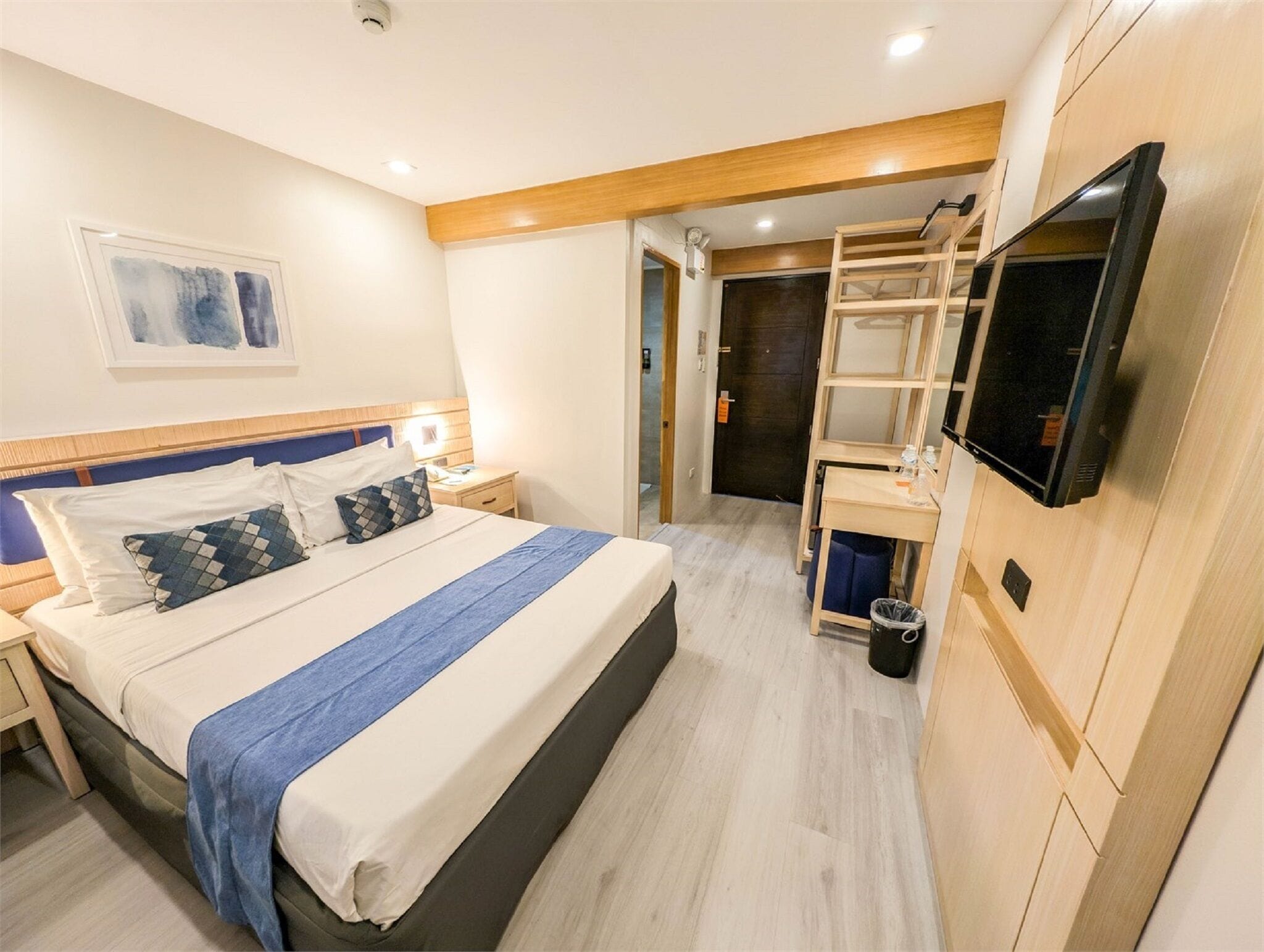 A hotel room with a bed, bedside table, TV, and a small desk area.