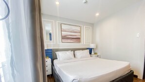 A bedroom with a large bed, a nightstand, a lamp, and a painting on the wall. - Uncle Tom's Cabin Hotel (Cebu City)