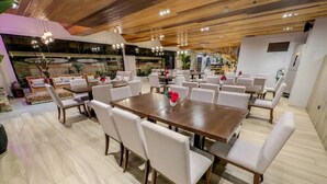A spacious dining area with a large wooden table surrounded by white chairs, a modern ceiling with wooden beams, and a view of the kitchen area. - Uncle Tom's Cabin Hotel (Cebu City)