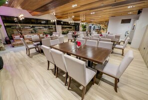 A spacious dining area with a large wooden table surrounded by white chairs, a modern ceiling with wooden beams, and a view of the kitchen area. - Uncle Tom's Cabin Hotel (Cebu City)