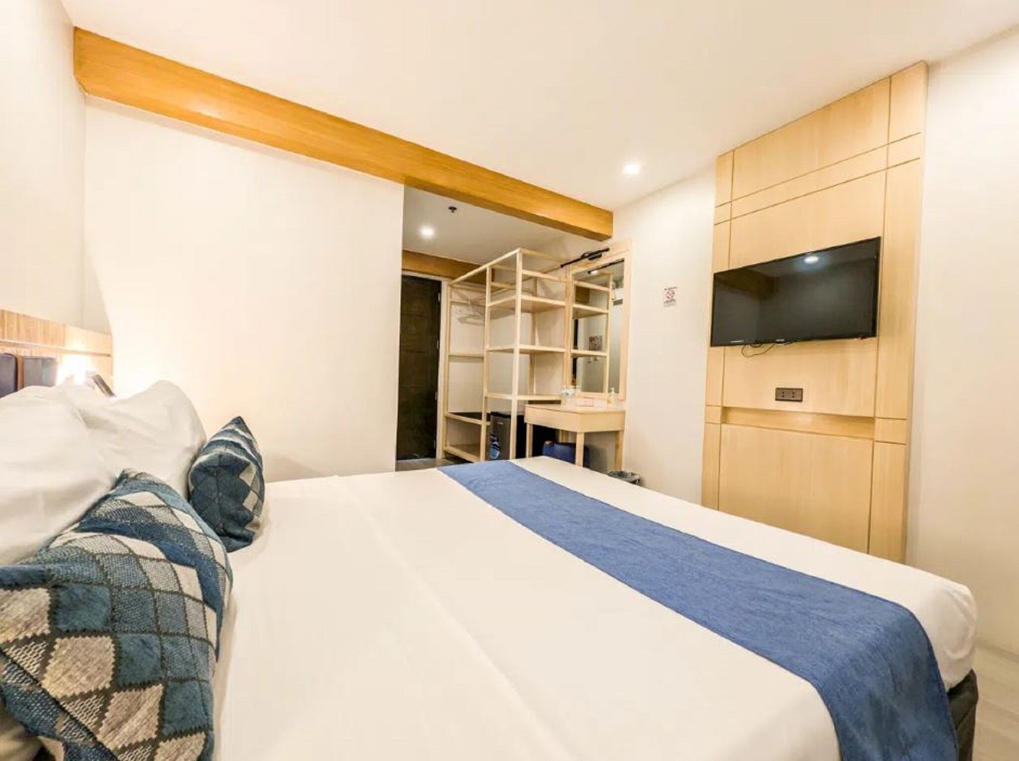 A bedroom with a bed, a TV mounted on the wall, and a wooden wardrobe.