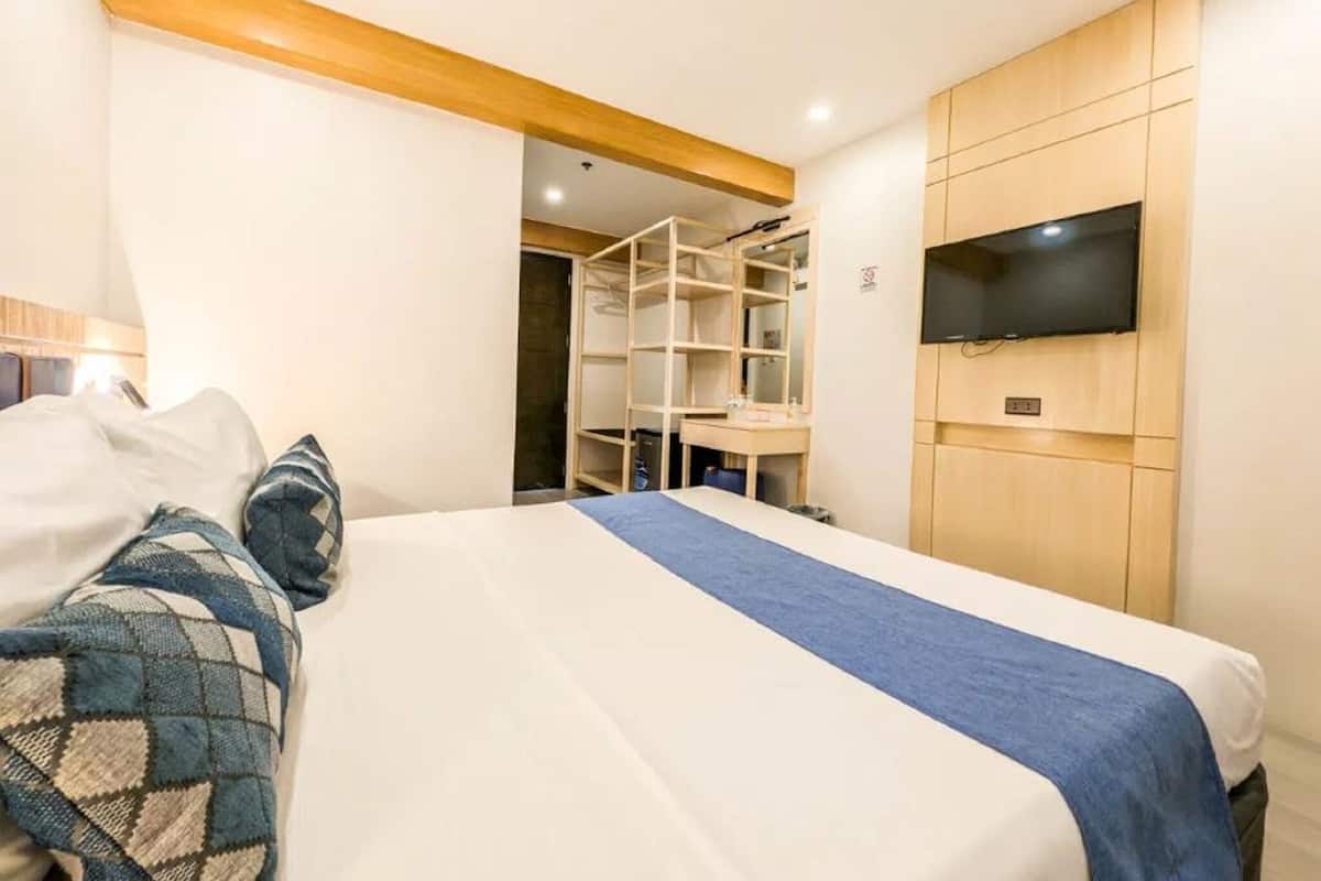 Une chambre à coucher avec un lit, un téléviseur fixé au mur et une armoire en bois.