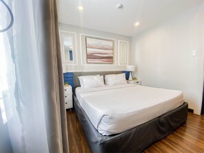 A bedroom with a large bed, a nightstand, a lamp, and a painting on the wall. - Uncle Tom's Cabin Hotel (Cebu City)