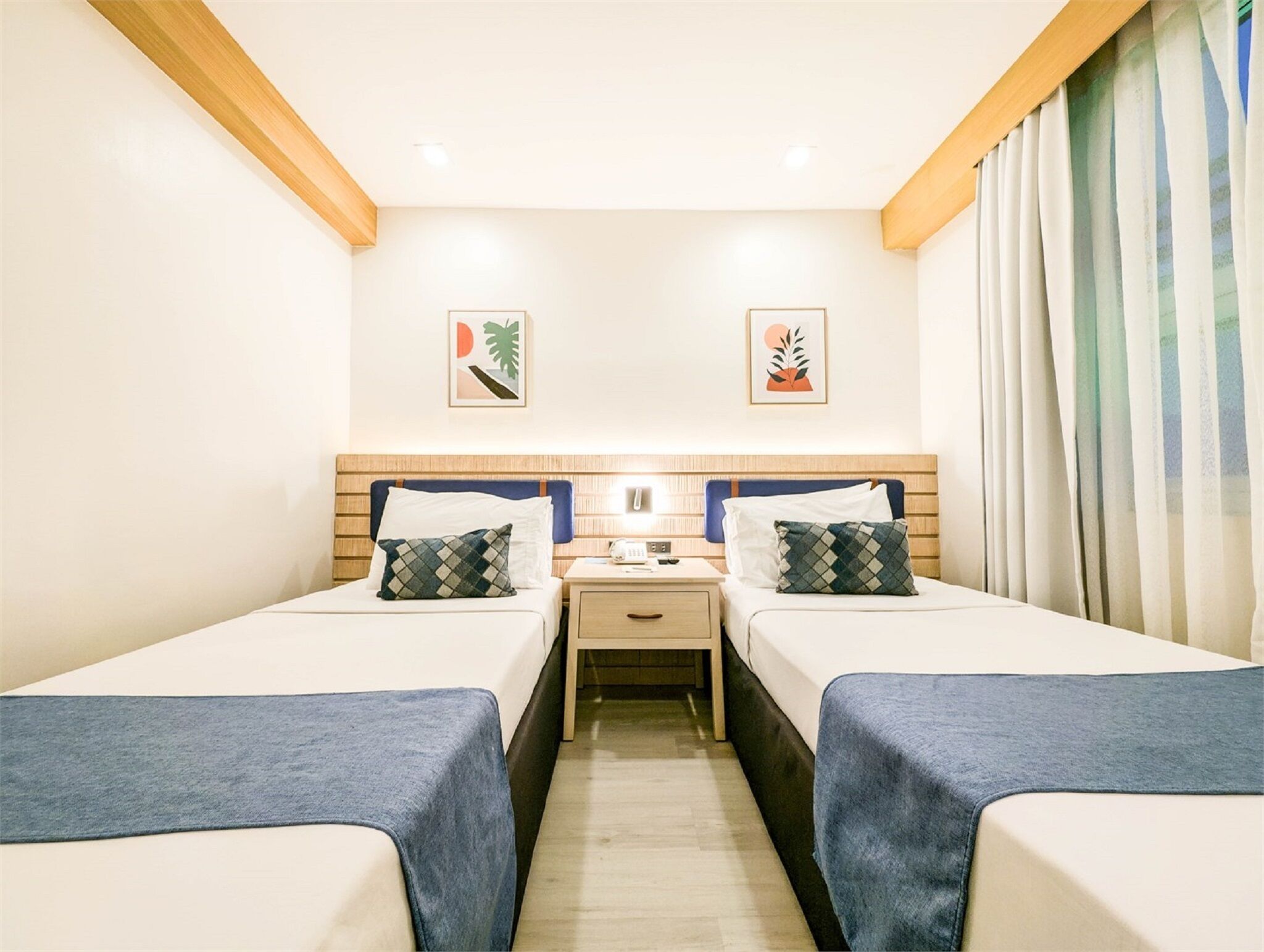 A hotel room with two single beds, a nightstand, a desk, and a window with curtains.