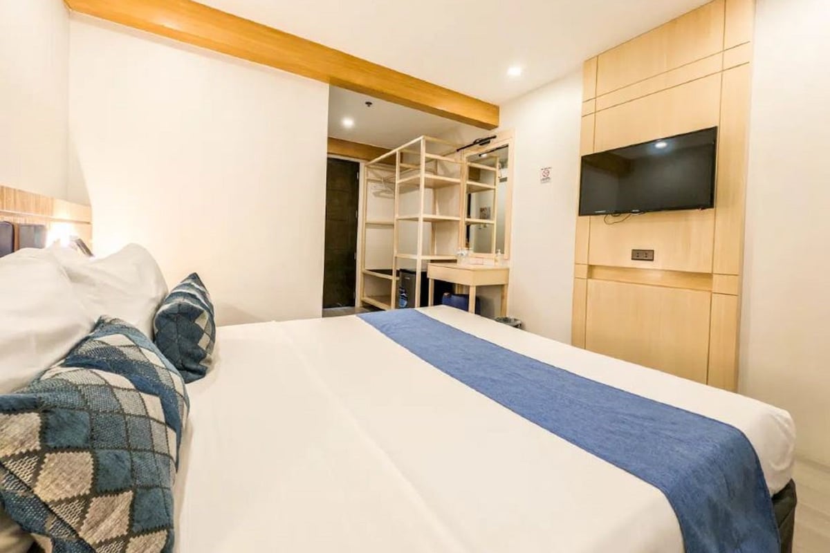 A bedroom with a bed, a TV mounted on the wall, and a wooden wardrobe.