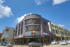 A multi-story building with a curved facade, storefronts on the ground level, and parked cars in front. - Rooms by Rocana (Kuantan)