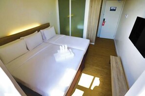 Quarto de hotel com uma cama, televisão, porta e chão de madeira.