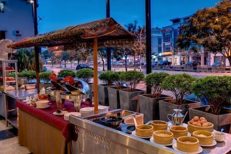 A buffet setup with various dishes and a canopy, surrounded by potted plants.. Rooms by Rocana