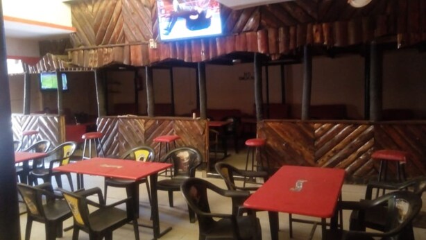 Ein Restaurant mit roten Tischen, schwarzen Stühlen, Holzvertäfelung an den Wänden und einem an der Wand befestigten Fernseher.